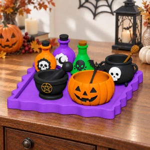 Puede incluir: Una bandeja morada con artículos de Halloween, incluyendo tres botellas pequeñas con etiquetas de calaveras y lunas, un mortero negro con mano y pentagrama, un cuenco con forma de calabaza y un caldero negro con una calavera y un cazo.