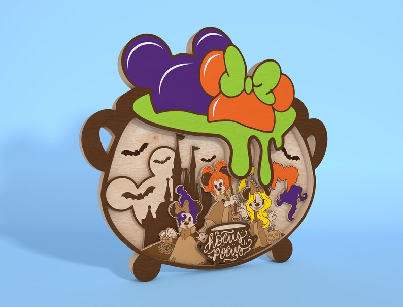 May include: A wooden Halloween decoration featuring a cauldron design with a purple Mickey Mouse ear hat, orange bow, and green slime. The cauldron has a layered design with bats, a castle, and cartoon characters. The text "Hocus Pocus" is also included.
