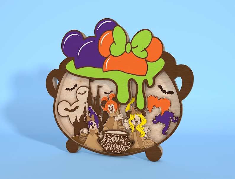 May include: Wooden Halloween-themed decoration in the shape of a cauldron. The cauldron features a green, orange, and purple bow, with a green slime effect. Inside are cartoon characters and the words "Hocus Pocus".