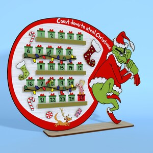 Puede incluir: Un calendario de adviento de madera rojo y verde con forma de c&iacute;rculo con una figura del Grinch sosteniendo una bolsa. El calendario tiene 25 puertas numeradas, cada una con una peque&ntilde;a imagen navide&ntilde;a. El texto "Count down to steal Christmas" est&aacute; escrito en la parte superior del calendario.