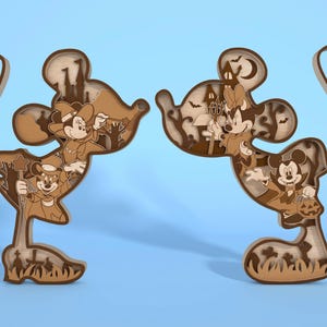 May include: Two wooden Mickey Mouse and Minnie Mouse figures in Halloween costumes. The figures are layered with a light brown and dark brown color scheme. The Mickey Mouse figure is holding a wand, and the Minnie Mouse figure is holding a trident.