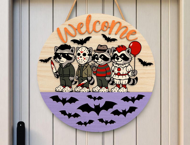 May include: Round wooden Halloween welcome sign featuring cartoon raccoons dressed as horror movie characters. The sign has a light wood grain background with the word "Welcome" in orange. A purple section at the bottom has black bat cutouts.