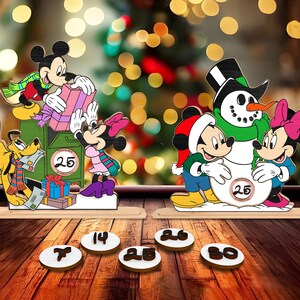 May include: A wooden Christmas advent calendar featuring Mickey Mouse and Minnie Mouse characters. The calendar has a green mailbox with a red number 25 on it. The characters are holding presents and standing on a wooden base. There are also wooden numbers 7, 14, 25, 26, and 30 on the table.