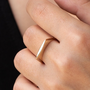 May include: A gold ring with a geometric, angular design. The ring is worn on the finger of a person's hand.