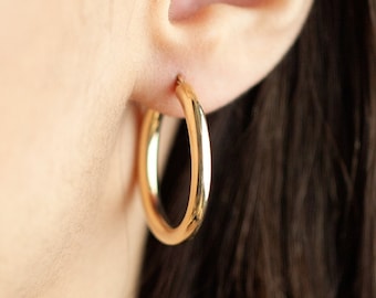 May include: Gold hoop earrings worn in a person's earlobe.