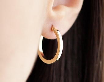 May include: Gold hoop earrings with a simple, polished finish. The earrings are worn in a person's ear.