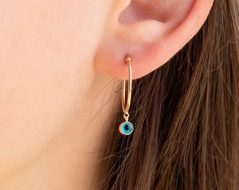 Puede incluir: Aretes de aro de oro con un pequeño dije de ojo turco azul que cuelga de la parte inferior.