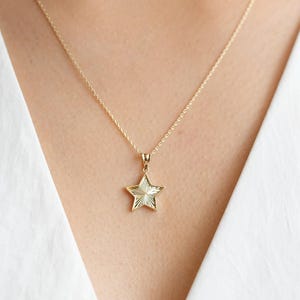May include: A gold chain necklace with a star-shaped pendant. The star has a textured surface and is a simple design.