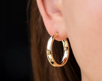 May include: Gold hoop earrings worn in a person's ear. The earrings are smooth and shiny.