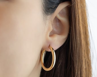 May include: Gold hoop earrings worn in a person's earlobe. The earrings are a simple, classic design.