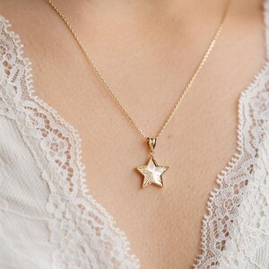 May include: A gold chain necklace with a star-shaped pendant. The star has a textured surface and is a simple design.