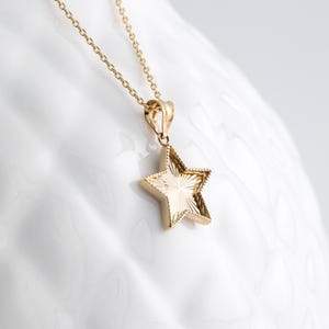 May include: A gold chain necklace with a star-shaped pendant. The star has a textured, sunburst design.