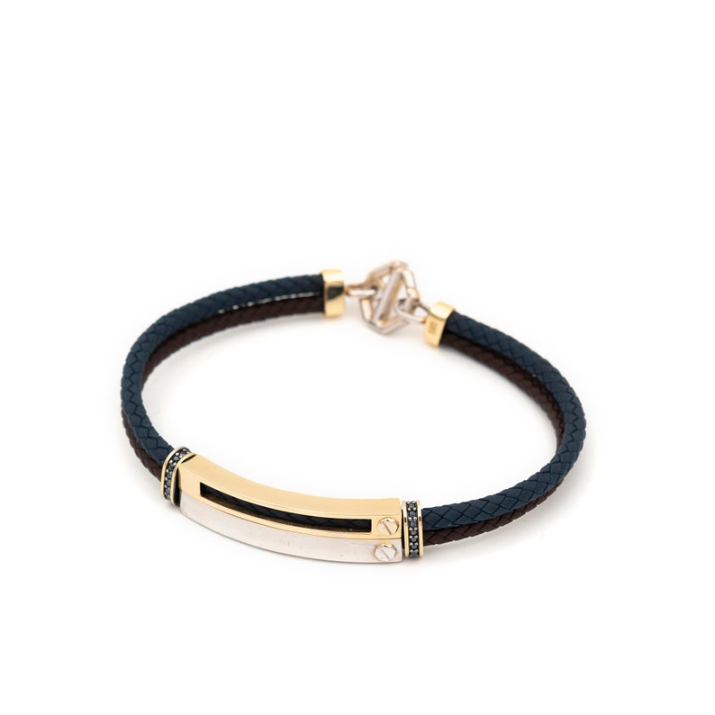 May include: A navy blue and brown braided leather bracelet with a gold and silver bar and black accents.