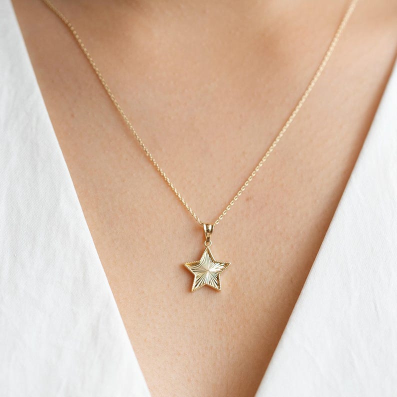 May include: A gold chain necklace with a star-shaped pendant. The star has a textured surface and is a simple design.