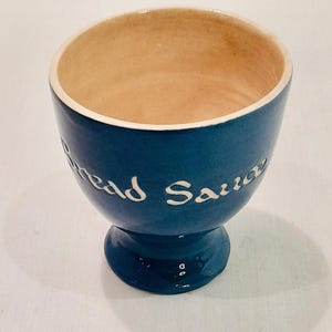 May include: A blue ceramic bowl with a white pedestal base. The bowl has the words "Bread Sauce" written on the side in white.