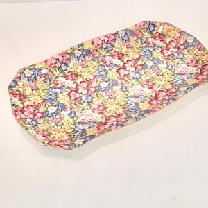 Op de afbeelding: Een rechthoekige serveerschaal met een bloemenpatroon in tinten roze, geel, blauw en groen. De schaal heeft een gouden rand.