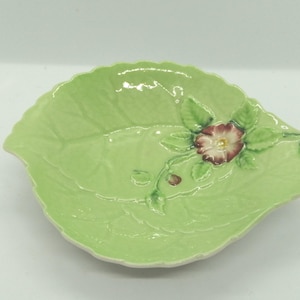 May include: A green ceramic dish shaped like a leaf with a pink flower and green leaves.