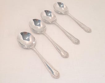 Può includere: Quattro cucchiai da zuppa d'argento disposti in diagonale. Ogni cucchiaio ha una coppa arrotondata e un manico dettagliato con un motivo decorativo. I cucchiai sono riflettenti, mostrando l'ambiente circostante.