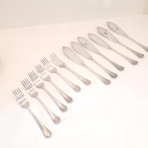 May include: A collection of silver-colored forks and butter knives arranged on a white surface. The utensils have a classic design with rounded handles and a polished finish. The image showcases a set of dining cutlery.