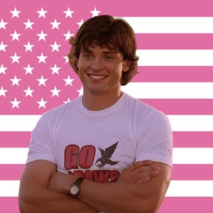 Peut inclure: Une personne porte un t-shirt blanc avec les mots "GO CROWS" et un graphisme d'oiseau. Le fond est un drapeau américain rose.