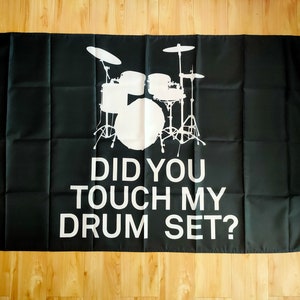May include: A black flag with a white silhouette of a drum set and the text "Did you touch my drum set?"