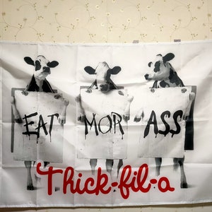 May include: A white flag with three black and white cows holding signs that say "EAT", "MOR", and "ASS". The text "Thick-fil-a" is written in red at the bottom of the flag.