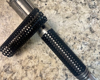Op de afbeelding: Een zilveren metalen lightsaber-handvat met een zwarte, geperforeerde, cilindrische hoes. De hoes is gedeeltelijk verwijderd, waardoor het ingewikkelde ontwerp van het handvat zichtbaar wordt.