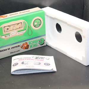 Puede incluir: Una consola de juegos portátil Nintendo Game & Watch verde y blanca con Donkey Kong 3. La consola está en su caja original con instrucciones. La caja es verde y blanca con el logotipo de Donkey Kong 3.