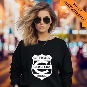 May include: Black sweatshirt with a white graphic of a police badge with the text "OFFICER CUSTOM #9323".