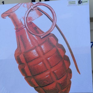 Puede incluir: Una impresión en lienzo de estilo pop art rojo y naranja de una granada de mano. La obra de arte presenta una representación detallada del cuerpo, el pasador y el anillo de la granada sobre un fondo blanco. El lienzo está etiquetado "Creative Canvas".