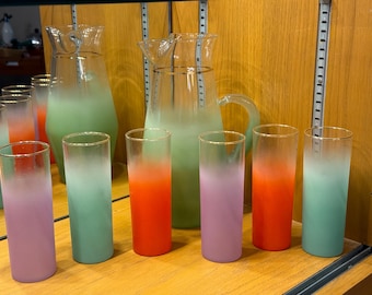 May include: A set of ombre glass tumblers and two pitchers. The tumblers are in shades of green, purple, and orange. The pitchers are green and clear.