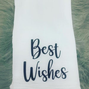 May include: White kitchen towel with black cursive text that reads "Best Wishes".