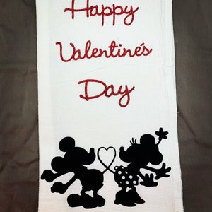 May include: White kitchen towel with red glitter text that reads "Happy Valentine's Day".  Black silhouette of Mickey Mouse and Minnie Mouse holding a heart.
