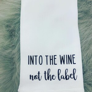 May include: White kitchen towel with black text that reads "Into the wine not the label".