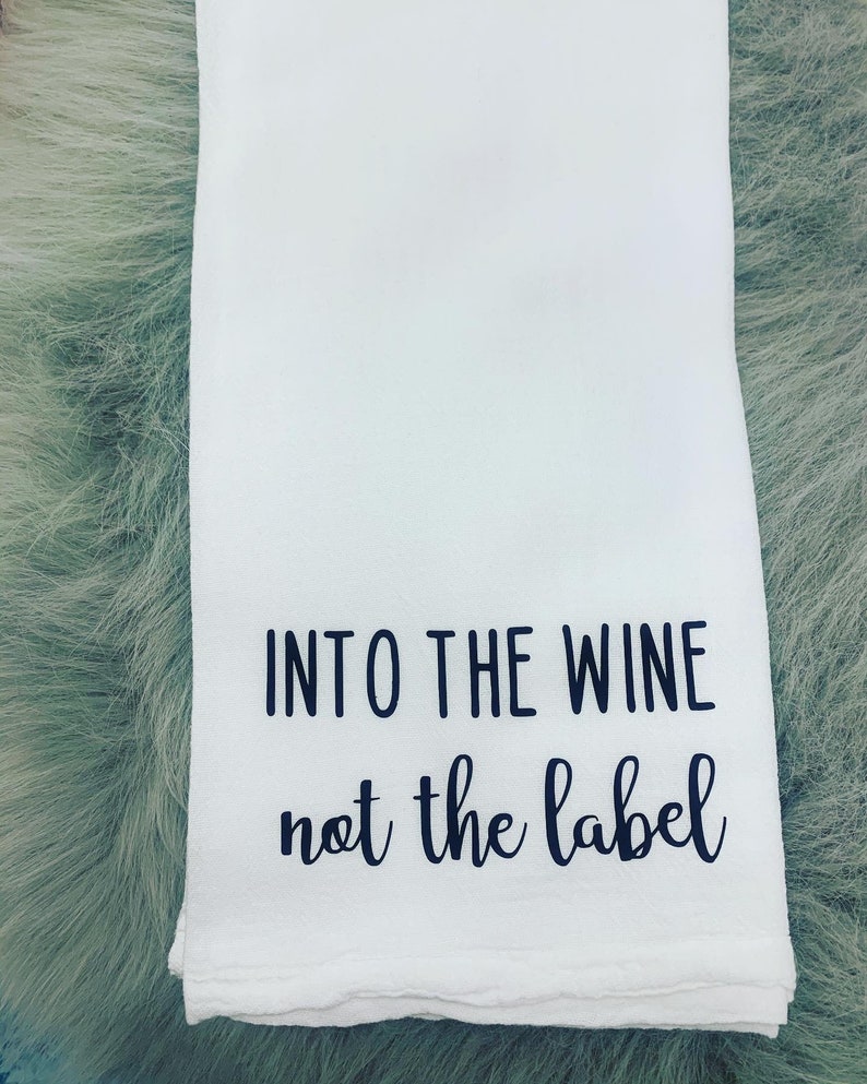 May include: White kitchen towel with black text that reads "Into the wine not the label".