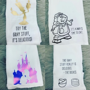 May include: Four white tea towels with different Disney-themed designs. The first towel features a gold candlestick with the text "Try the gray stuff, it's delicious!" The second towel features a black and white illustration of Cogsworth from Beauty and the Beast with the text "It's always time to eat." The third towel features a pink and purple castle with a silhouette of Belle and the Beast with a holographic finish. The fourth towel features a black and white illustration of two bowls and a stack of plates with the text "The gray stuff really is delicious. - The Dishes."