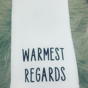 May include: White kitchen towel with black text that reads "Warmest Regards".
