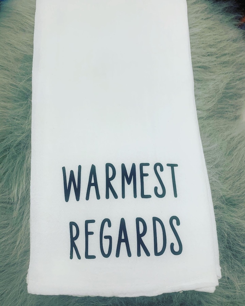 May include: White kitchen towel with black text that reads "Warmest Regards".
