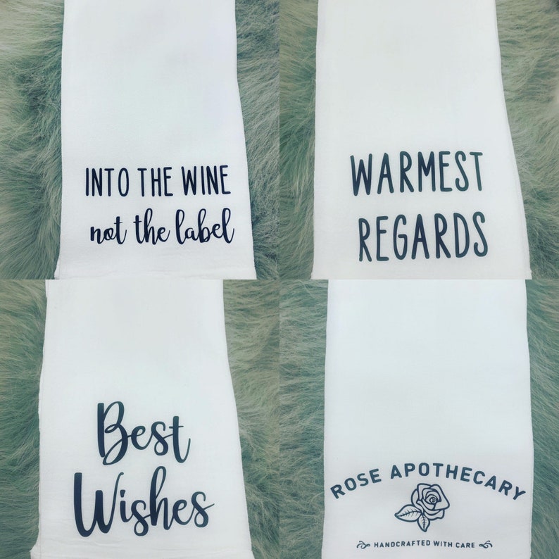 May include: Four white tea towels with black text. The first towel says "INTO THE WINE not the label". The second towel says "WARMEST REGARDS". The third towel says "Best Wishes". The fourth towel says "ROSE APOTHECARY" with a small rose graphic and the text "HANDCRAFTED WITH CARE".