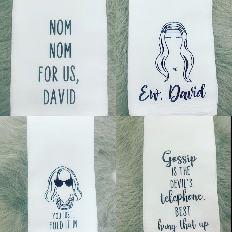 May include: Four white tea towels with black text and illustrations. The first towel says "Nom Nom For Us, David". The second towel has a black illustration of a woman with long hair and the text "Ew, David". The third towel has a black illustration of a woman with sunglasses and the text "You Just... Fold It In". The fourth towel says "Gossip Is The Devil's Telephone. Best Hang That Up".