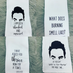 May include: Four white kitchen towels with black text and a black silhouette of a man's face. The text on the towels reads: "I am both shocked and impressed", "What does burning smell like?", "I have asked you thrice now for a towel - David Rose", and "If you say "fold in the cheese" one more time..."