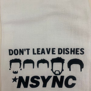 May include: White kitchen towel with black text that reads "Don't leave dishes *NSYNC" with five black silhouettes of men's heads above the text.