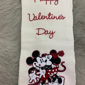 May include: White kitchen towel with red glitter lettering that says "Happy Valentine's Day".  A red and black cartoon image of Mickey Mouse and Minnie Mouse kissing is in the bottom center of the towel.