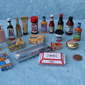 May include: Miniature food items including bottles of ketchup, mustard, and hot sauce, along with a coffee cup, cheese, and a chocolate bar. The items are arranged on a light blue surface with glitter.