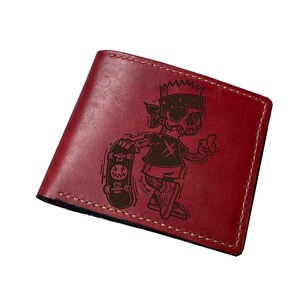 May include: Red leather wallet with a black and white engraved design of a cartoon character skateboarding.