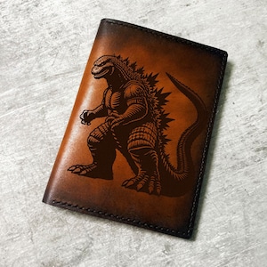 May include: A brown leather passport holder with a black embossed image of Godzilla.