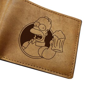 May include: A brown leather wallet with a laser-engraved image of a cartoon character holding a beer mug. The character has yellow skin, blue eyes, and a big smile.