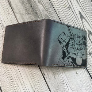 May include: A brown leather wallet with a black and white graphic of a robot on the front.