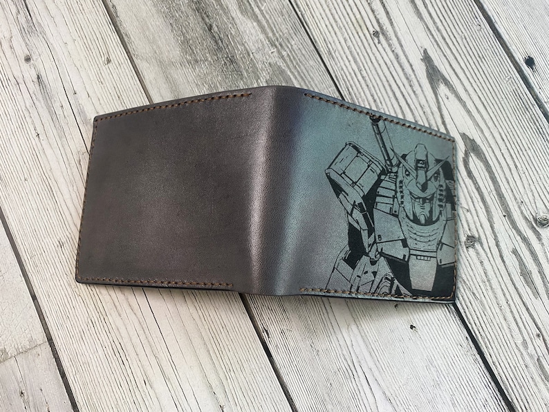 May include: A brown leather wallet with a black and white graphic of a robot on the front.