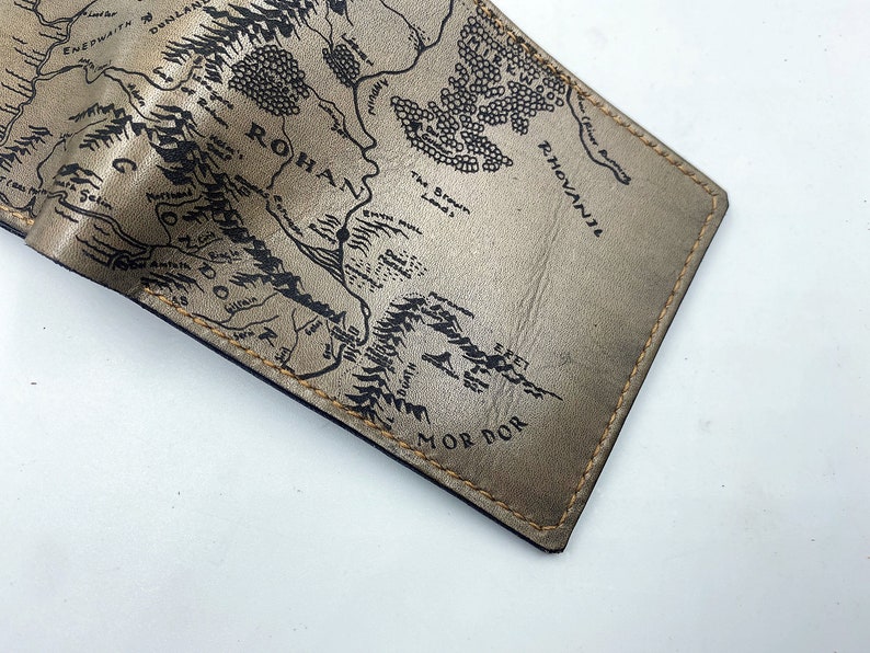 May include: A gold leather wallet with a black and white map of Middle-earth printed on the front. The map includes the text "Mordor", "Rohan", and "Rh&oacute;vanion".